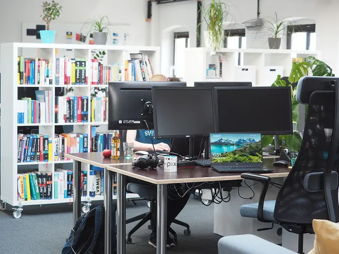Arbeitsbereich bei e-pixler mit mehreren Monitoren und Regalen voller Bücher.