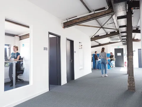 Büroflur bei e-pixler mit Mitarbeitern, die an ihren Arbeitsplätzen sitzen oder sich unterhalten.