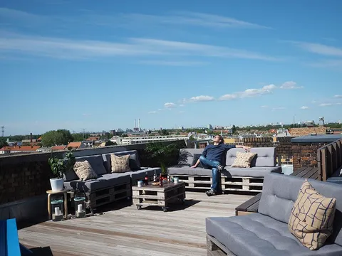 Dachterrasse bei e-pixler mit Palettenmöbeln, Kissen und einem weiten Blick über die Stadt.