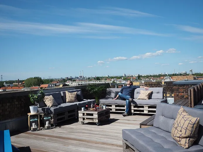 Dachterrasse bei e-pixler mit Palettenmöbeln, Kissen und einem weiten Blick über die Stadt.