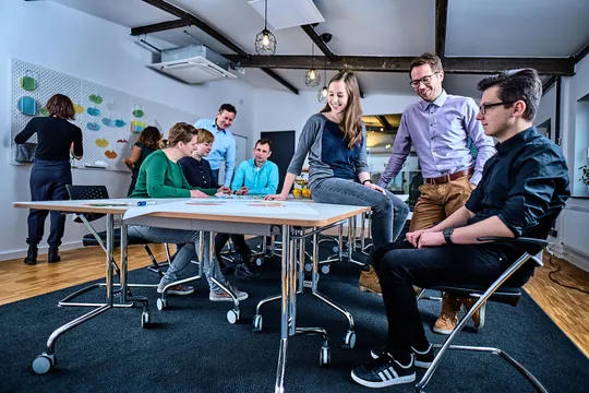 e-pixler-Mitarbeiter bei einer Team-Besprechung in einem modernen Büro mit Whiteboards und Schreibtischen.