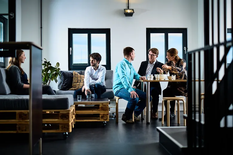 e-pixler-Mitarbeiter unterhalten sich in einem modernen Lounge-Bereich mit Palettenmöbeln und Fensterfront.